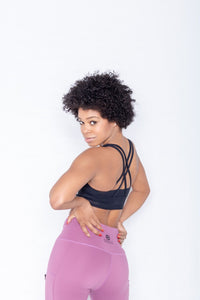 Shakolo crossover bra in black and high waist leggings in purple back view model with arms on waist looking backwards intently