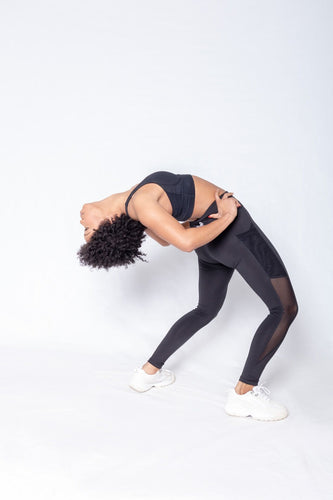 Shakolo crossover bra in black and mid waist leggings in black side view model bending backwards