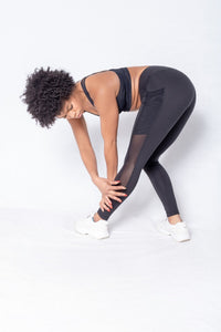 Shakolo crossover bra in black and mid waist leggings in black side view model bending over and model touching leg