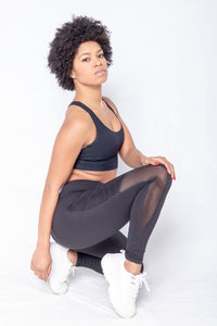 Shakolo crossover bra in black and mid waist leggings in black side view model squating with pointed toe