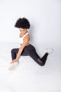 Shakolo crossover bra in white and mid rise leggings in black side view model sitting on ground with legs bent